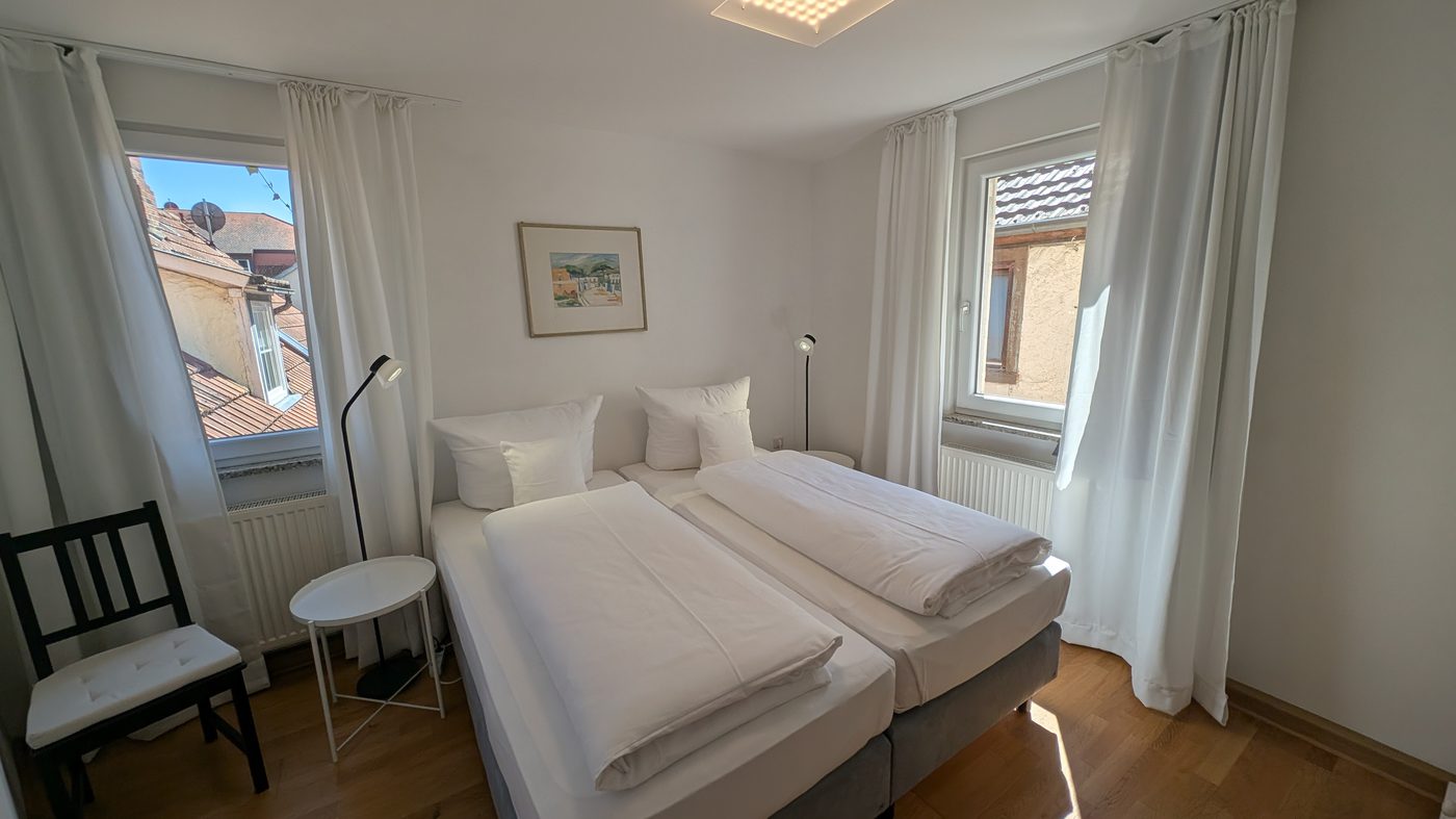 Helles Schlafzimmer mit Doppelbett, zwei Fenstern und Sonnenlicht