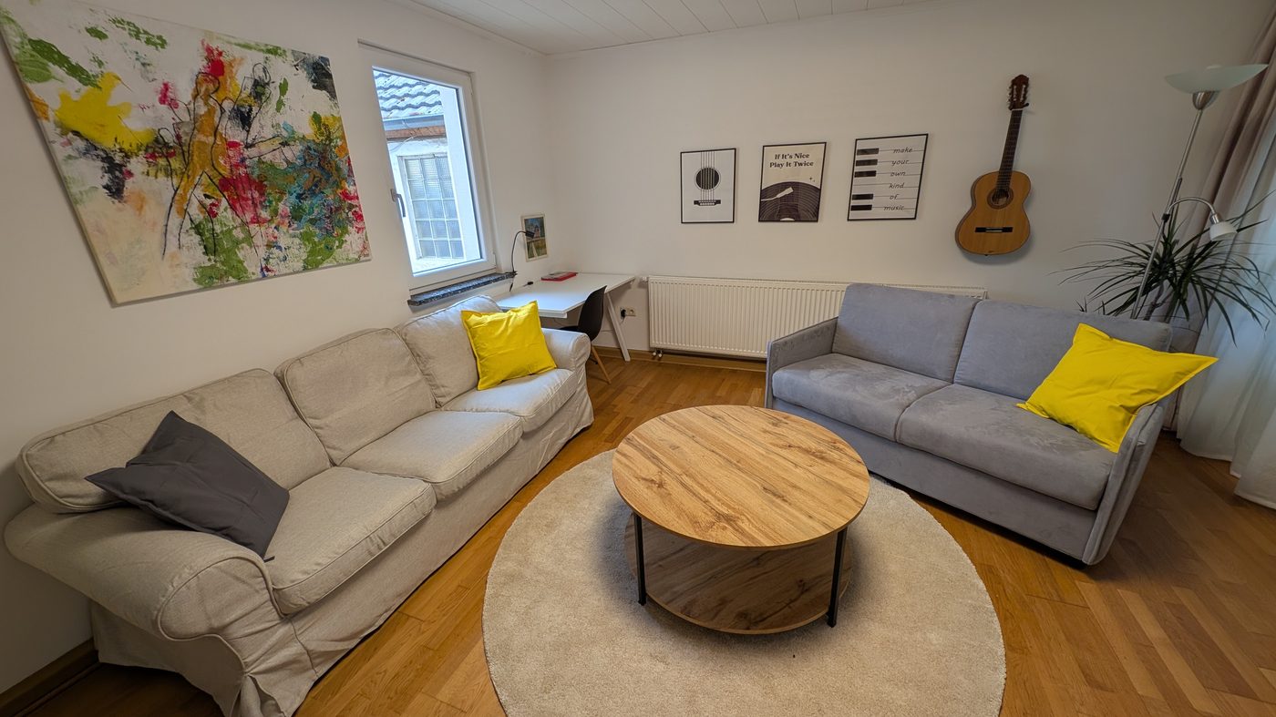 Wohnzimmer mit Gitarre an der Wand, zwei Sofas und buntem Kunstbild